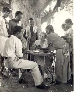 Dr Ida B Scuddder sits at a table under a tree with men and women around her