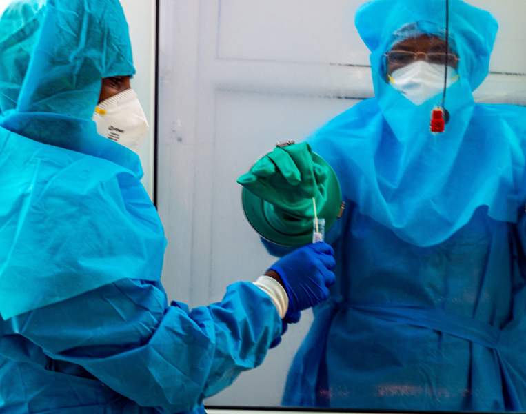 person inside the booth places the swab into the tube held by person outside